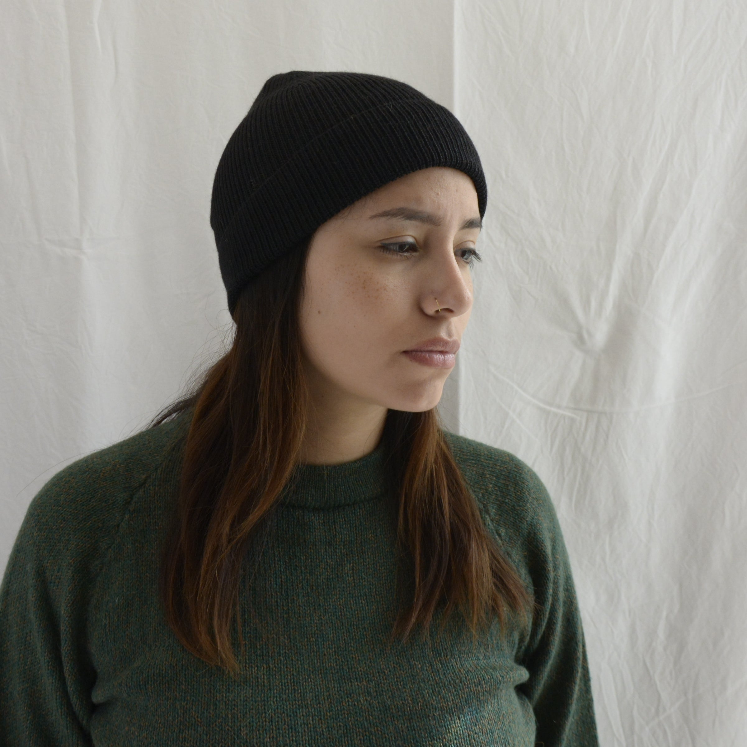 Woman_wearing_alpaca_en_Peru_black_beanie_and_green_round_neck_sweater_and_looking_down_beside