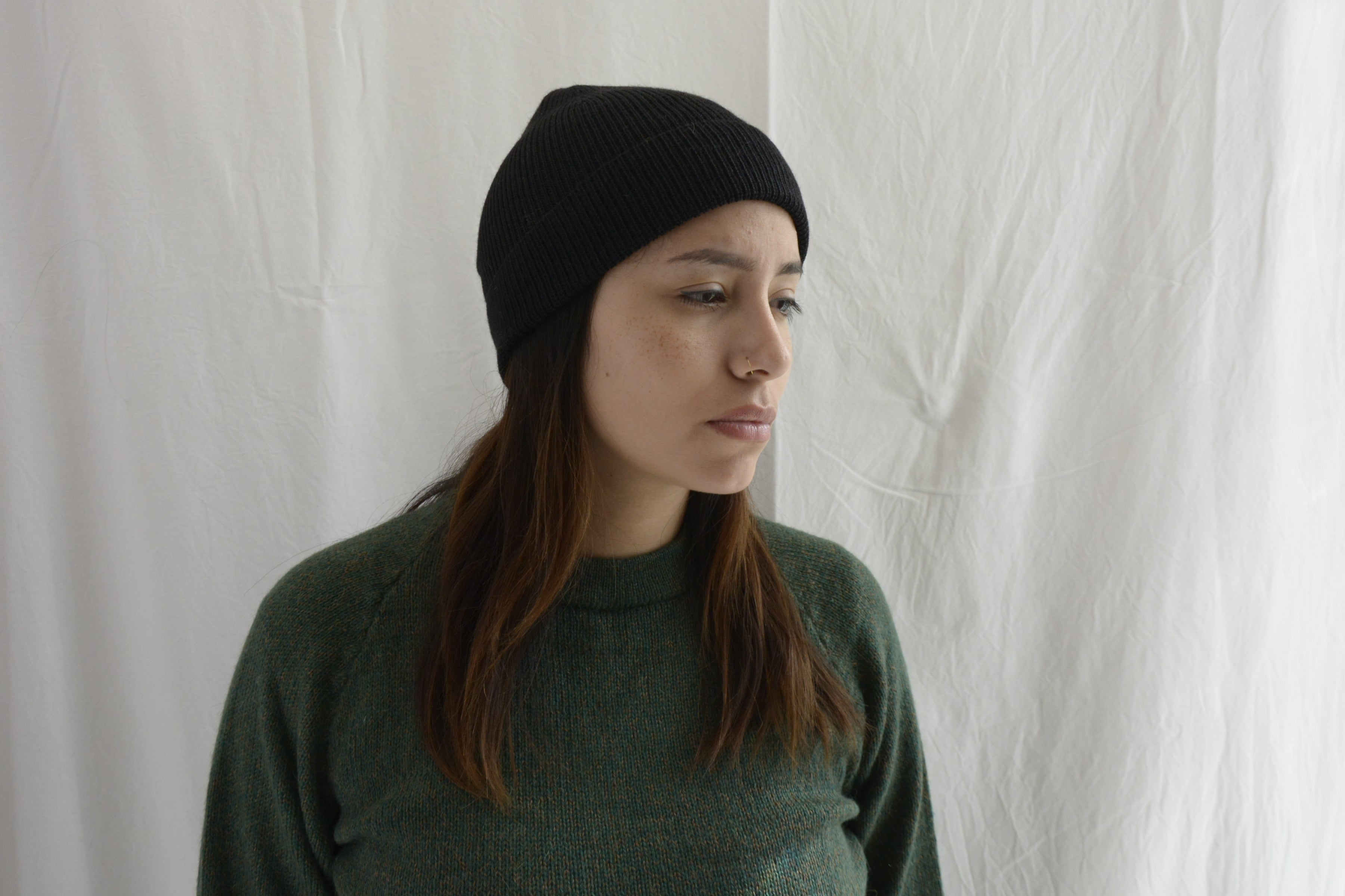 Woman_wearing_alpaca_en_Peru_black_beanie_and_green_round_neck_sweater_and_looking_down_beside