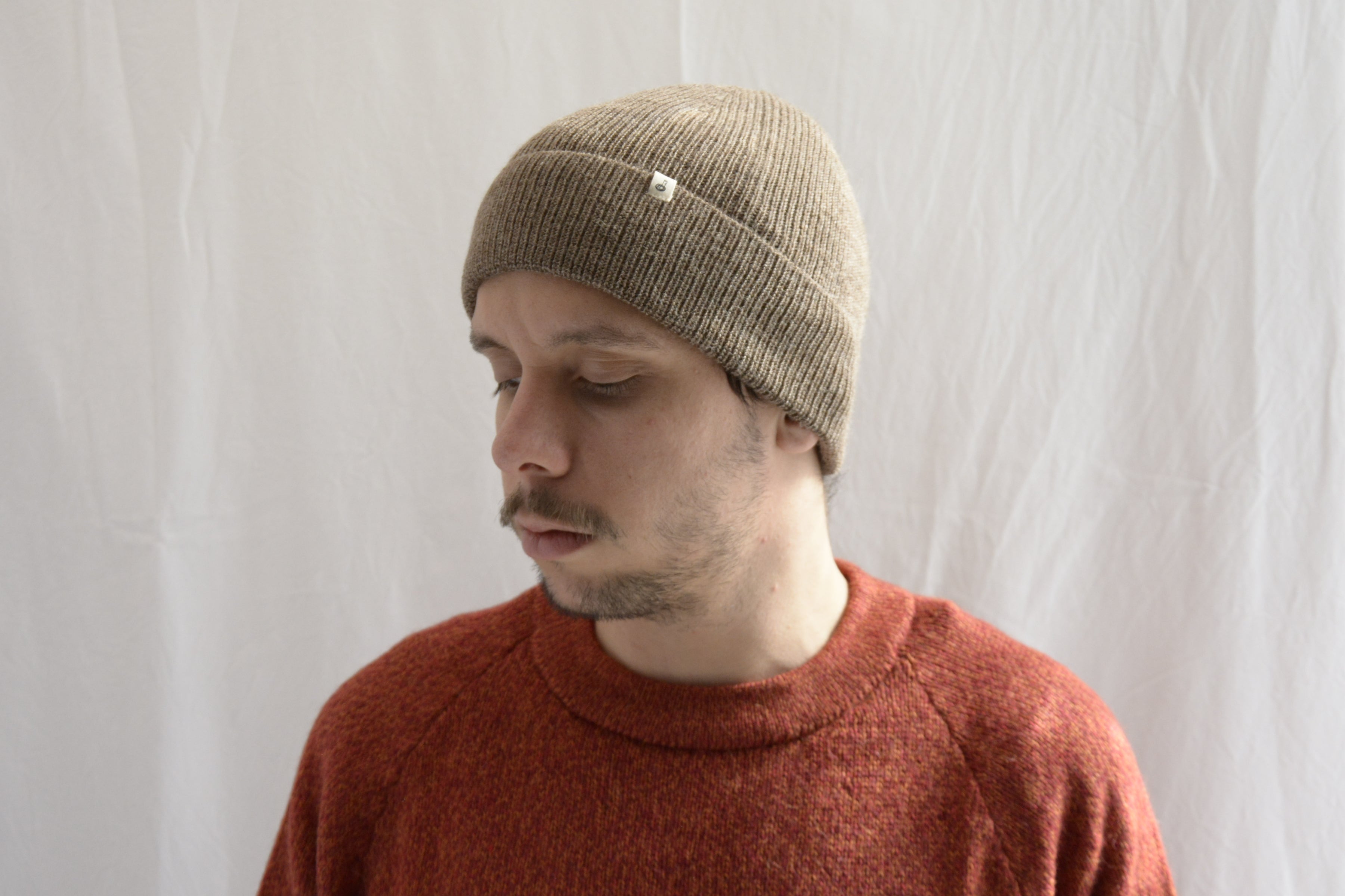 Man_wearing_alpaca_en_peru_coffee_beanie_and_orange_round_neck_sweater_and_looking_down_beside