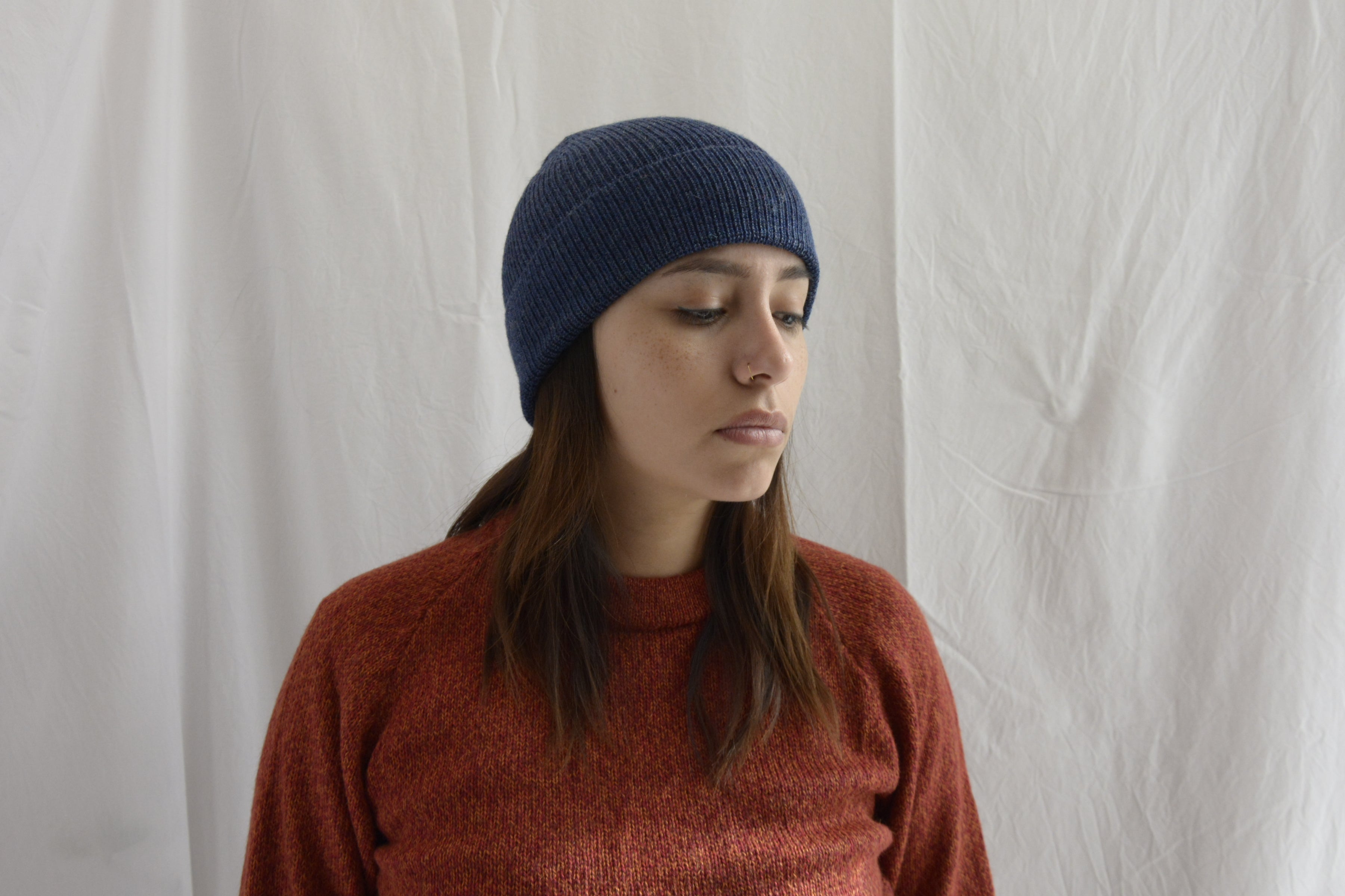 Woman_wearing_alpaca_en_peru_steel_blue_beanie_and_orange_round_neck_sweater_and_looking_down_beside