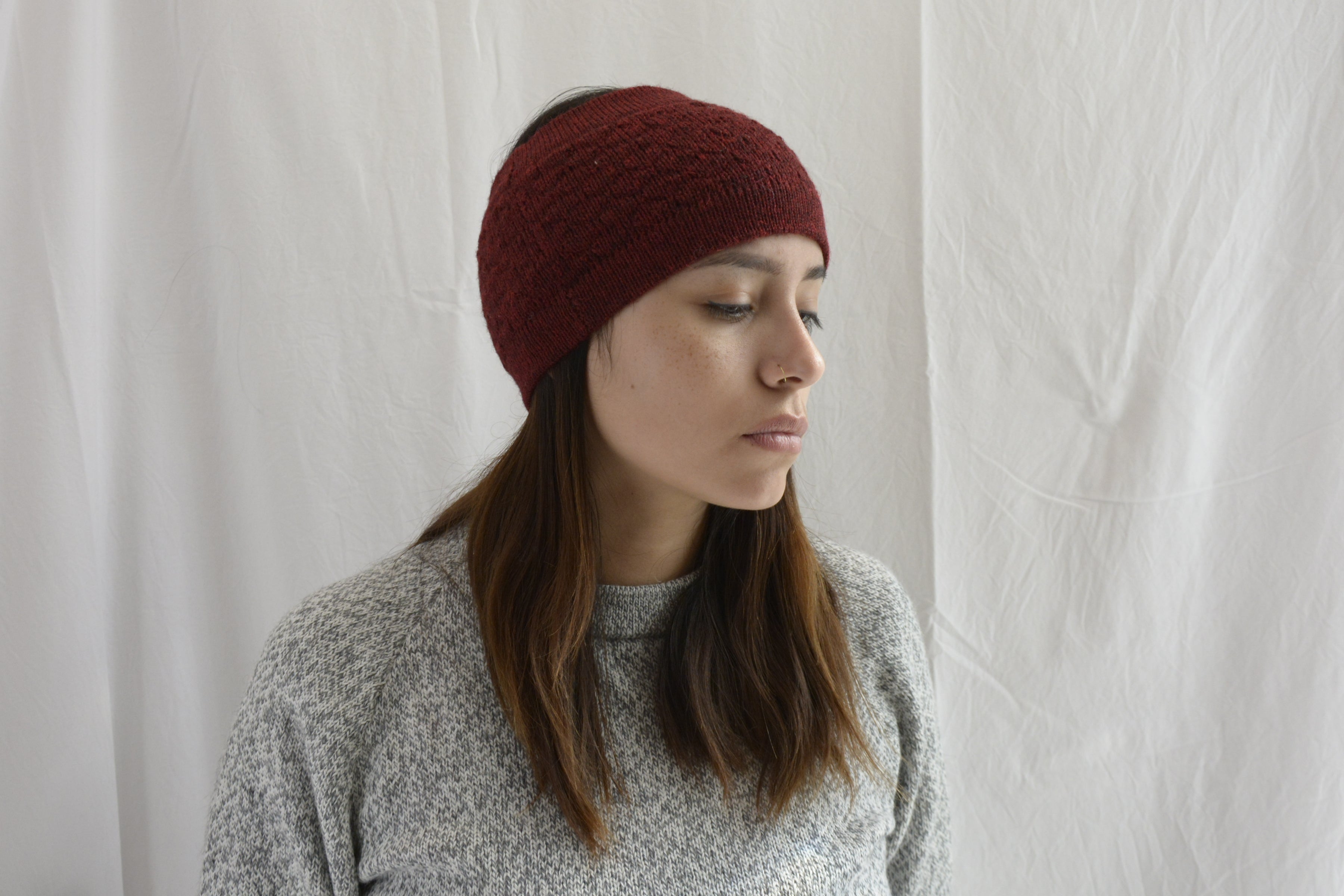 Woman_wearing_alpaca_en_peru_brick_red_head_band_and_light_grey_rond_neck_sweater_and_look_down_beside